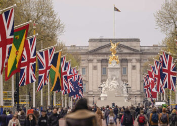 People walk along the Mall where British and Commonwealth countries flags have been put, ahead of the coronation of Britain's King Charles III, in London, Thursday, April 27, 2023. (AP Photo/Alberto Pezzali)